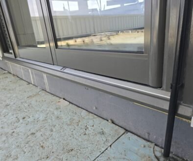 Close-up of a dark gray metal-framed sliding glass door at ground level, showing the bottom sill and a concrete exterior surface nearby.