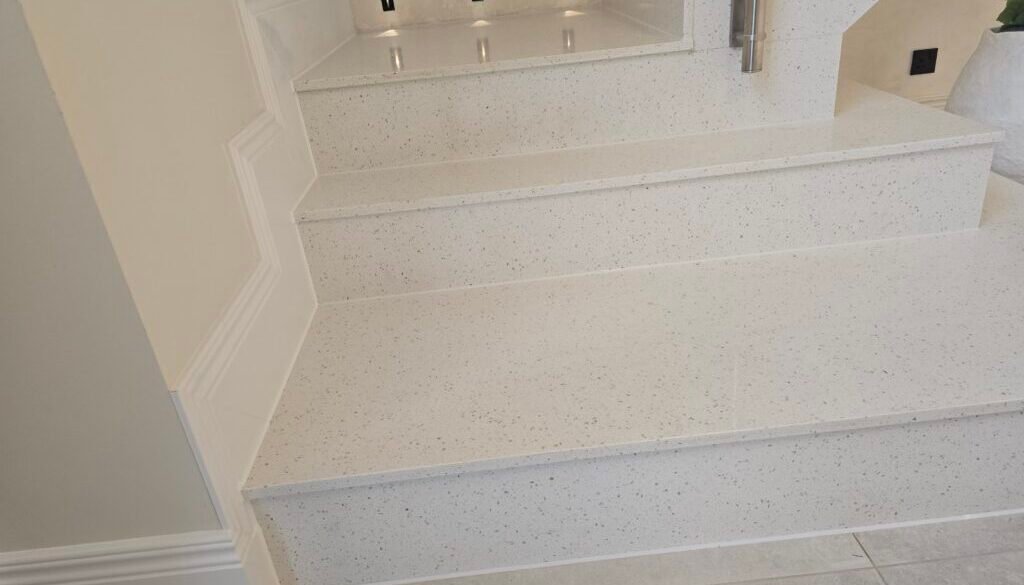 White speckled terrazzo staircase with wide steps and a raised landing; a metal handrail is on the right side.