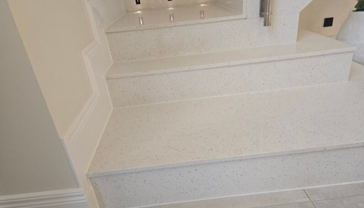 White speckled terrazzo staircase with wide steps and a raised landing; a metal handrail is on the right side.