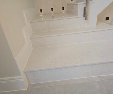 White speckled terrazzo staircase with wide steps and a raised landing; a metal handrail is on the right side.