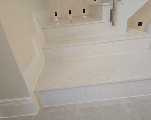 White speckled terrazzo staircase with wide steps and a raised landing; a metal handrail is on the right side.