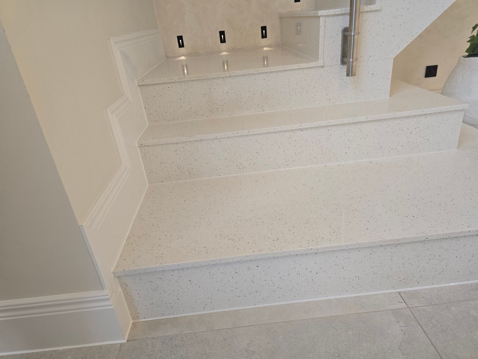 White speckled terrazzo staircase with wide steps and a raised landing; a metal handrail is on the right side.
